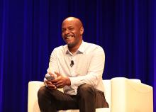 A man smiles while sitting in a chair and holding a phone