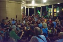 People pack together on a porch playing fiddles and basses