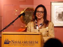 a brown-haired woman with glasses stands behind a podium