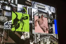 Two dancers suspended against a side of a building with video projections in the background