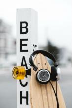 Skateboard leaning against post that says beach with headphones hanging on it