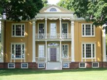 the facade of a yello multi-story Federal-style house with a columned porch and multiple windows