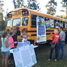 Teens at table next to school bus with posters on it.