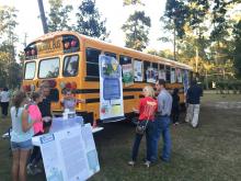 girls at a display next to a school bus with adults looking on