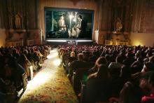 A movie plays on the screen of an ornate theater as an audience watches