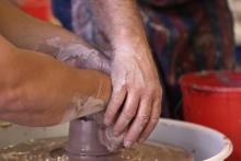 three hands shape a vessel on a pottery wheel