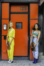 Two standing women holding violins in front of red background