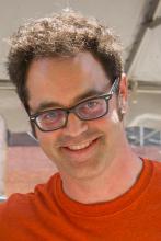 A photo of a man with curly brown hair and an orange shirt.