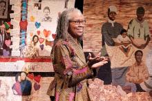A woman stands smiling with a quilt hanging behind her.