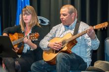 woman and man sitting down playing guitar together