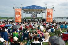 Front view of the outdoor stage with audience members sitting on blankets and folded chairs.