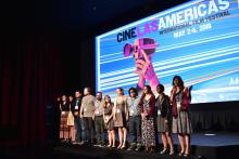 A group of people standing on a stage with a screen that says Cine Las Americas behind them