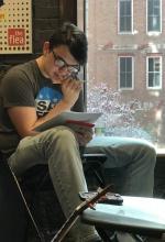  a young man sits in a chair near a window studying pages in a notebook