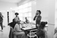 High school students sit around a table while one student stands and speaks
