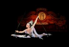 a woman circus aerialist suspended in a split in front of a red circus sarasota sign