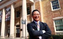 an Asian-American man with glasses posing out a college building