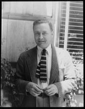 Headshot of F. Scott Fitzgerald. He is standing outside in front of a window and smiling.