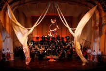 Orchestra on stage performing, while acrobats are also performing on the same stage. 