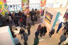 a crowd gathers in an exhibit space with graffiti-inspired artwork is on view