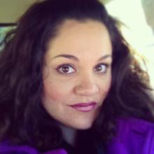 a Latina woman with long wavy hair, a nose ring, and a purple shirt