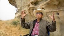 Grant Bulltail wearing a ranch hat and glasses standing on a rocky landscape