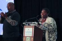 a young African American woman behind a podium with a sign language interpreter to her left