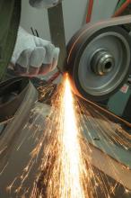 Sparks fly from a grinder belt in a blacksmith studio