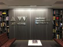 NEA's logo on a gray wall with a bookshelf on each side. 