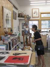 an Asian woman looking at art on paper in an art-filled studio space