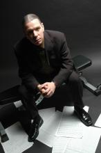 Man in dark suit sitting on weight bench with sheet music scattered on ground