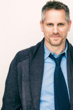 headshot of the actor Jonno Roberts a white man with short hair wearing a blue cardigan sweater