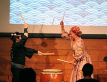 two women play a taiko drum standing on either side of it