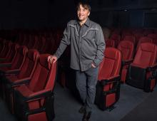 Man standing while holding onto red theater seats