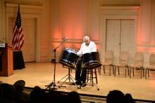 A man sits on a stage behind three steel drums