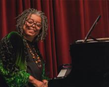 Mary Watkins smiling and sitting in front of a piano.