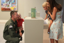 a family with the dad in military uniform looks at an art object on a plinth