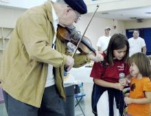 An elderly man playing violin to a couple of children.