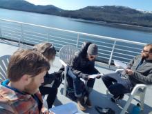 People reading papers sitting on the deck of a ferry in Alaska