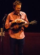 Man smiling holding a mandolin.