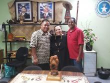 A woman stands between two men amidst cultural objects from the Northern Mariana Islands