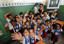 Dark-haired man stands with waving school children