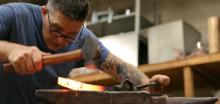 Man looks closely at a blade he is forging