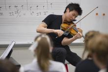 A man performs on the violin in a classroom while students watch.