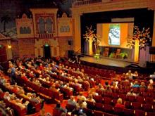 Bird's eye view of the inside of a theater. Stage decorated and room filled with people. 
