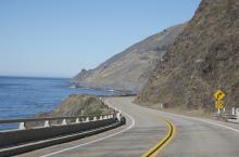 Empty road with the Pacific ocean to the left and mountains to the right.