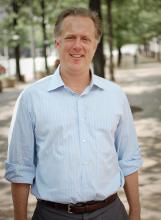 A man in a light blue collared shirt stands outside on a sidewalk