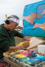 A man in bandana does a watercolor painting in front of a colorful bus