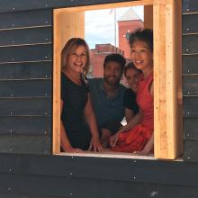 Four people look out the squared window of a small studio space