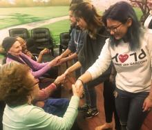 Group of standing teens hold hands with group of seated older adults