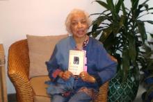 Ruby Dee on her couch holding up a copy of Ernest Gaines A Lesson Before Dying